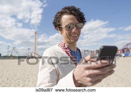 Stock Photo - Mid adult man texting on smartphone at beach. Fotosearch