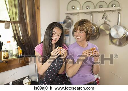 Mid adult woman and teenage girl in kitchen, eating snack View Large Photo Image Stock Image - Mid adult woman and teenage girl in kitchen, eating snack. Fotosearch