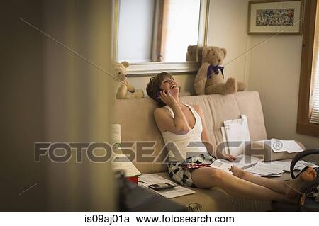 Mid adult woman sitting on sofa, using mobile phone View Large Photo Image Stock Image - Mid adult woman sitting on sofa, using mobile phone. Fotosearch