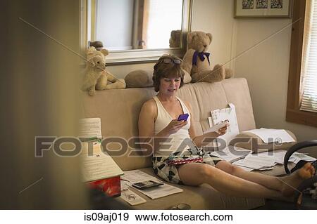 Mid adult woman sitting on sofa, using mobile phone View Large Photo Image Stock Photo - Mid adult woman sitting on sofa, using mobile phone. Fotosearch
