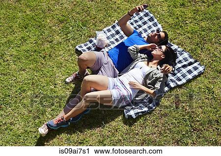 Stock Image - Overhead view of couple taking self portrait on picnic blanket. Fotosearch