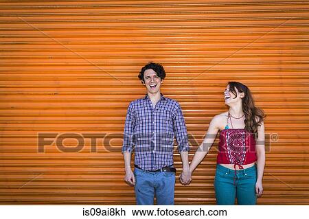 Stock Image - Portrait of couple in front of orange shutter. Fotosearch