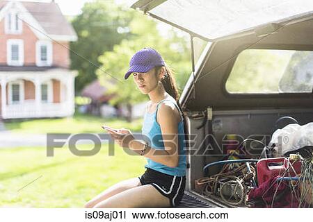 Stock Image - Portrait of teenage girl, sitting on open car boot. Fotosearch