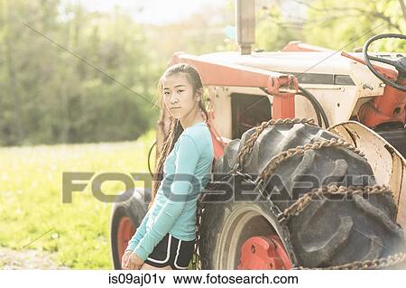 Stock Photo - Portrait of teenage girl standing beside tractor. Fotosearch