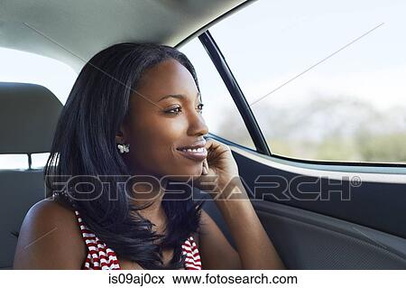 Stock Photo - Portrait of young woman gazing through car backseat window. Fotosearch