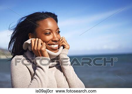 Stock Photography - Portrait of young woman holding rollneck on sweater at beach, Malibu, California, USA. Fotosearch