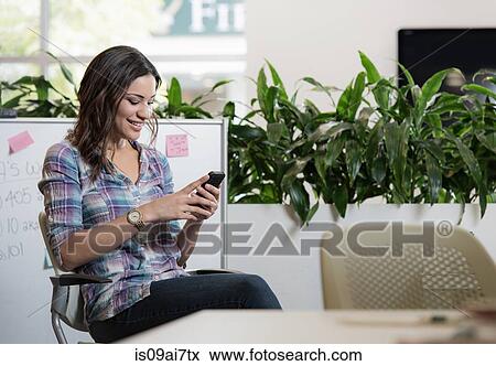 Stock Photo - Relaxed young businesswoman texting on smartphone in office. Fotosearch