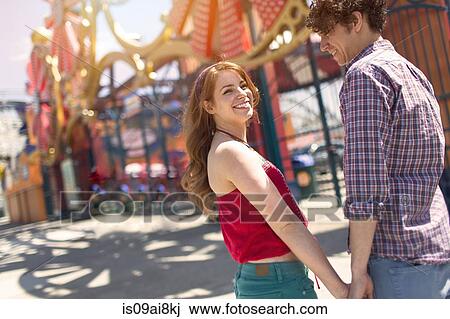Stock Image - Romantic couple holding hands at amusement park. Fotosearch