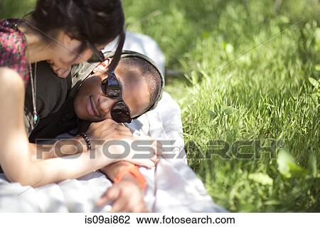 Stock Image - Smiling young couple on picnic blanket in park. Fotosearch