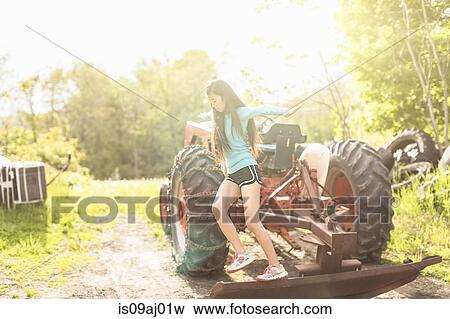 Stock Photo - Teenage girl balancing on tractor. Fotosearch