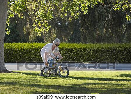 Three year old boy learning to cycle with grandmother in park View Large Photo Image Stock Photo - Three year old boy learning to cycle with grandmother in park. Fotosearch