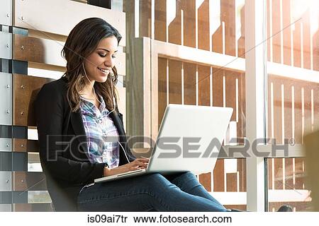 Stock Photography - Young businesswoman listening to laptop earphones in office. Fotosearch