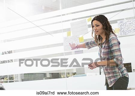 Stock Image - Young businesswoman presenting ideas on office window. Fotosearch