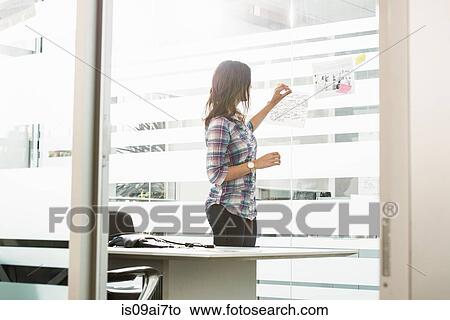 Young businesswoman putting post it notes on office window View Large Photo Image Picture - Young businesswoman putting post it notes on office window. Fotosearch