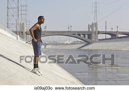 Young male runner taking a break on city riverbank View Large Photo Image Picture - Young male runner taking a break on city riverbank. Fotosearch