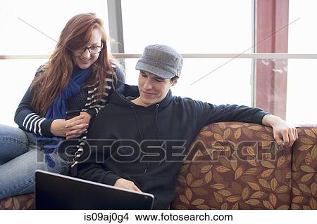 Young man and woman sitting on sofa with laptop View Large Photo Image Picture - Young man and woman sitting on sofa with laptop. Fotosearch