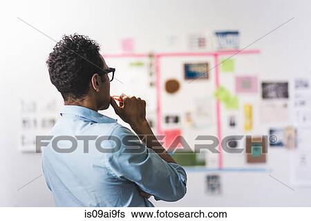 Stock Photograph - Young man studying wall of notes at office. Fotosearch