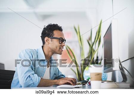 Picture - Young man working at computer in office. Fotosearch