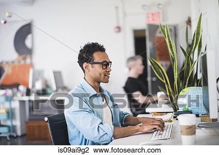 Stock Image - Young man working at computer in office. Fotosearch