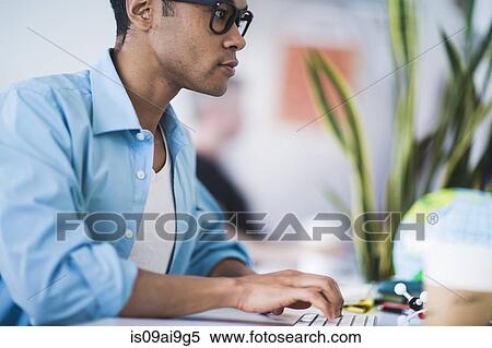 Stock Photography - Young man working at computer in office. Fotosearch