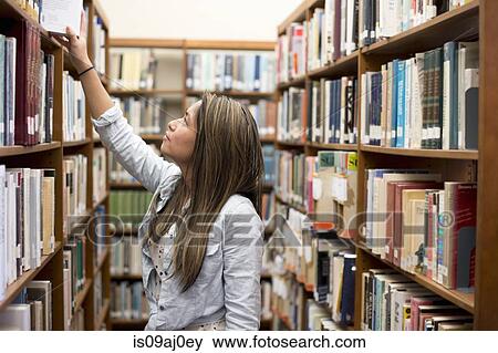 Stock Photo - Young woman choosing book in library. Fotosearch