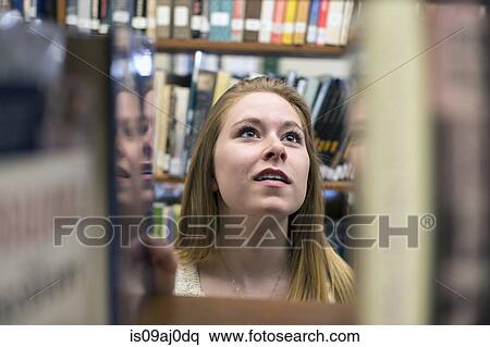 Stock Photography - Young woman choosing book in library. Fotosearch