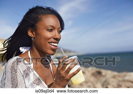 Picture - Young woman drinking fruit juice at beach, Malibu, California, USA. Fotosearch
