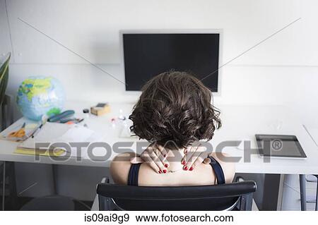 Stock Photo - Young woman massaging her neck at desk. Fotosearch