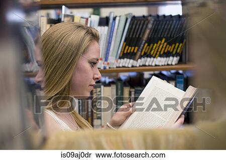 Stock Photography - Young woman reading book in library. Fotosearch