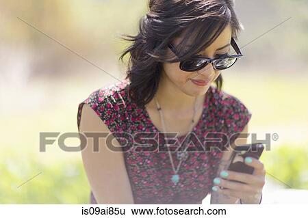 Young woman sitting in park with smartphone View Large Photo Image Stock Photograph - Young woman sitting in park with smartphone. Fotosearch