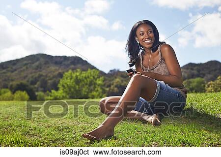 Stock Photograph - Young woman sitting on grassy hill. Fotosearch