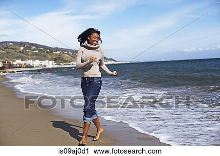 Stock Image - Young woman walking barefoot on beach, Malibu, California, USA. Fotosearch
