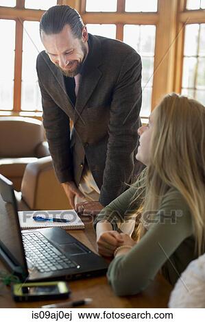 Stock Image - Young woman with laptop talking to teacher. Fotosearch