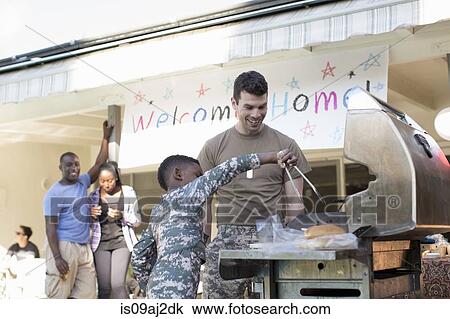 Stock Image - Boy barbecuing burgers with male soldier at homecoming party. Fotosearch