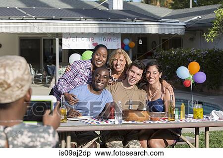 Stock Photography - Boy photographing male soldier with family and friends at homecoming party. Fotosearch