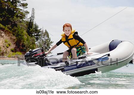 Stock Image - Boy steering speeding motor dinghy at sea. Fotosearch