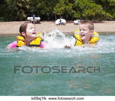 Stock Image - Brother and sister play fighting and splashing in sea. Fotosearch