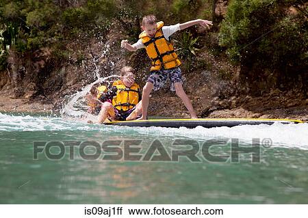 Stock Image - Brothers and sister splashing from paddleboard at sea. Fotosearch