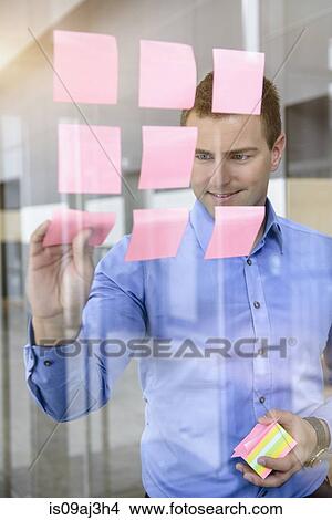 Picture - Businessman arranging post it notes on office window. Fotosearch