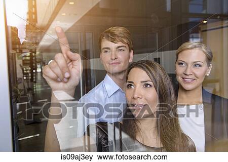 Businesswoman pointing out of glass window to colleagues View Large Photo Image Stock Photo - Businesswoman pointing out of glass window to colleagues. Fotosearch