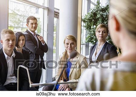 Businesswomen and men listening to speaker in office conference room View Large Photo Image Stock Photograph - Businesswomen and men listening to speaker in office conference room. Fotosearch