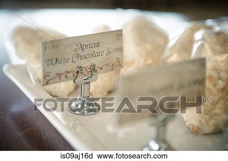 Stock Image - Close up of labeled scones on tray in cafe. Fotosearch