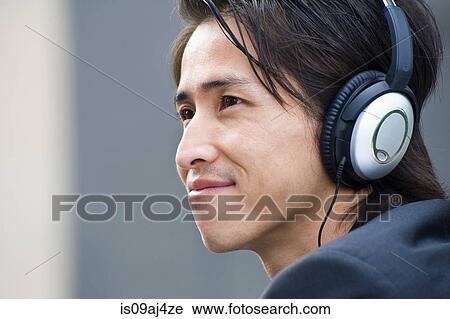 Stock Image - Close up of mid adult businessman listening to music on headphones. Fotosearch