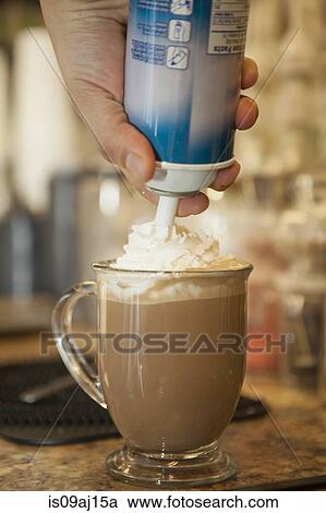 Stock Image - Close up of waiter squirting whipped cream onto cup of hot chocolate. Fotosearch