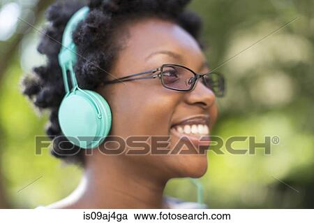 Close up of young woman in park listening to headphones View Large Photo Image Stock Image - Close up of young woman in park listening to headphones. Fotosearch