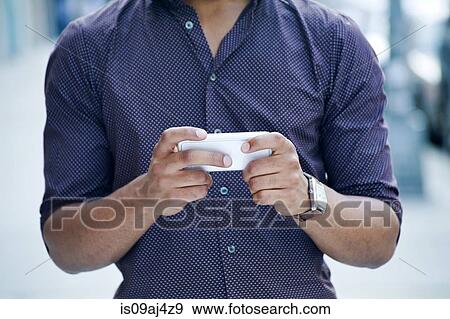 Stock Photo - Cropped shot of young man on city street using smartphone. Fotosearch