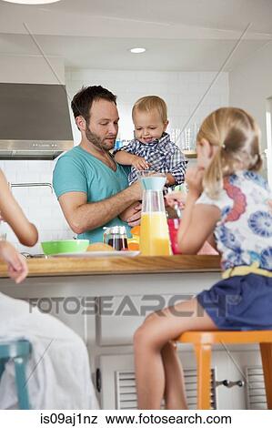 Stock Photo - Father multi tasking breakfast with son and daughters. Fotosearch