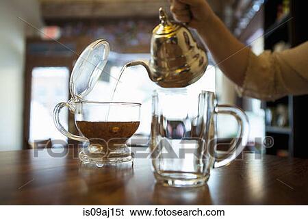 Stock Photograph - Female hand pouring tea on cafe counter. Fotosearch