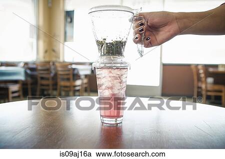 Stock Image - Female hand with iced herbal tea and filter in cafe. Fotosearch