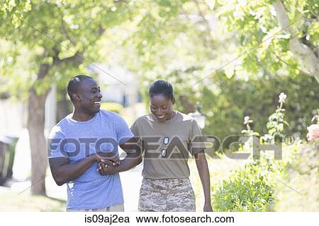 Stock Image - Female soldier holding husband's hand whilst strolling on homecoming. Fotosearch